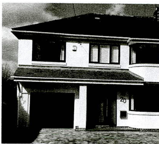 A black and white photograph showing the front exterior of a two-story detached house with an attached garage and driveway.