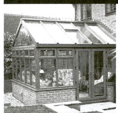 A photograph showing a conservatory or sunroom extension attached to a residential property, featuring a brick base and a pitched glass roof with skylights.