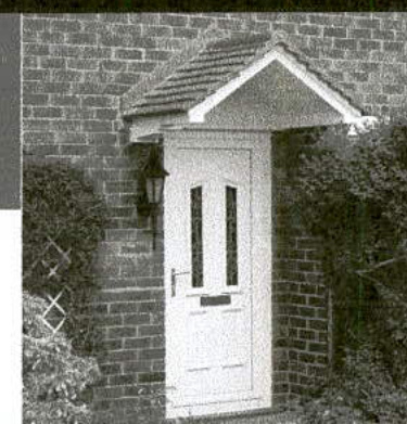 A black and white photograph showing a white front door with a small tiled porch canopy, set in a brick wall with bushes on either side.