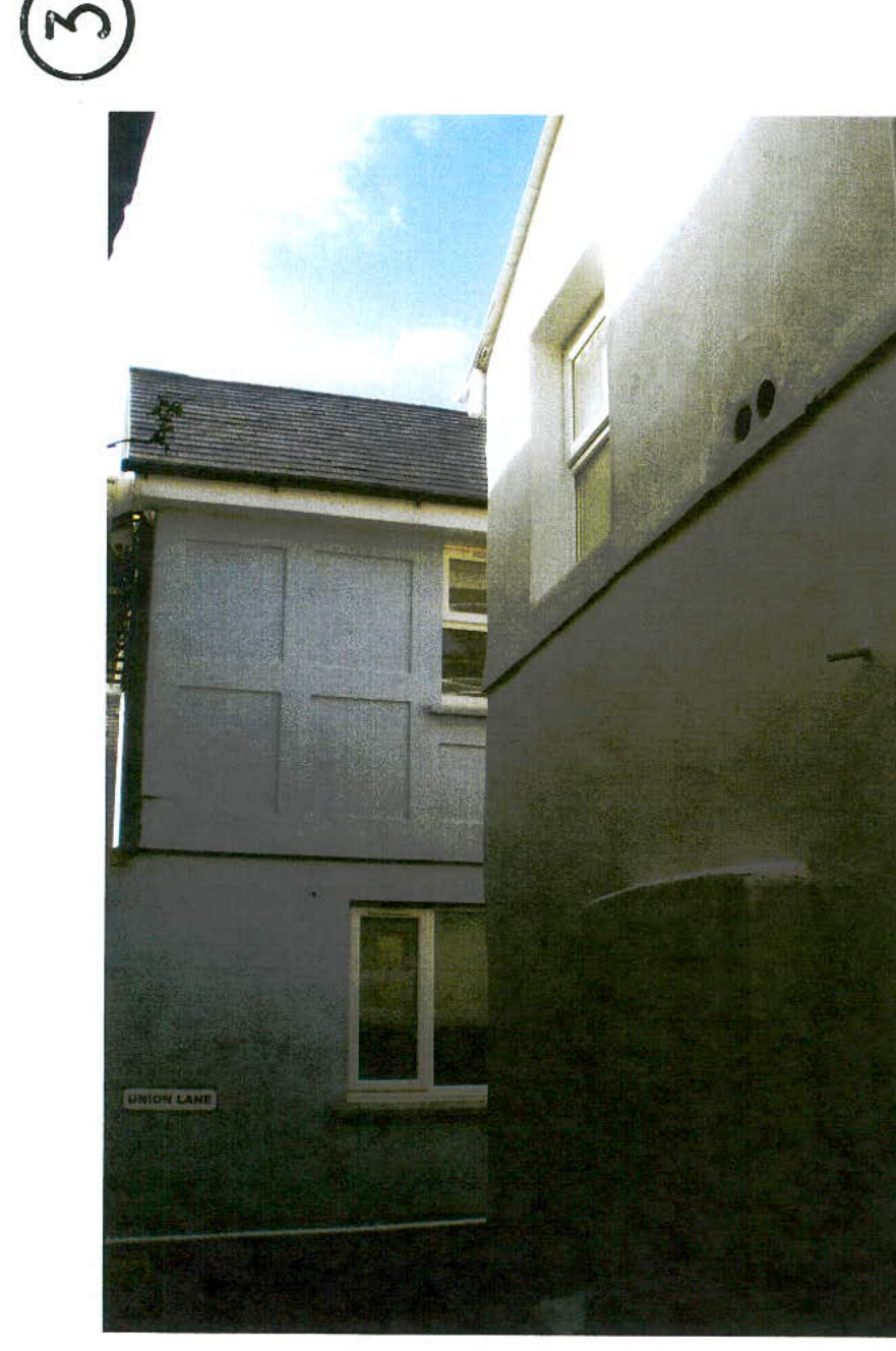 A grainy photograph showing the side elevation of a white two-story residential building on Union Lane, viewed from a narrow gap between structures.