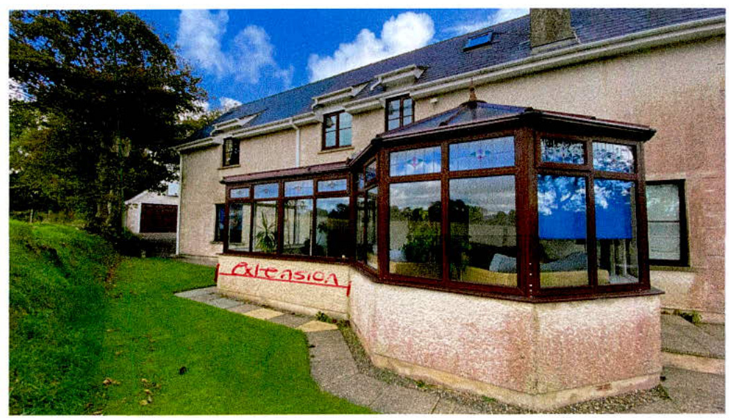 A photograph showing a large conservatory extension attached to a residential house with the word 'Extension' written in red on the low wall.