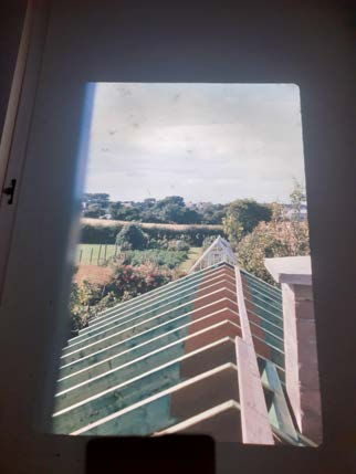A photograph taken through a window frame showing a green tiled roof in the foreground and a rural landscape with fields and trees in the distance.