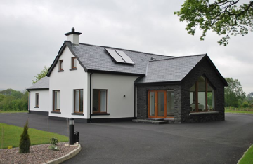A modern detached house featuring white rendering and stone cladding, set in a rural environment with a large paved driveway and solar panels on the roof.