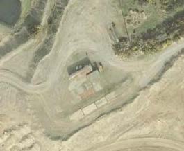 Aerial satellite view of a rural site featuring a small structure and dirt tracks.