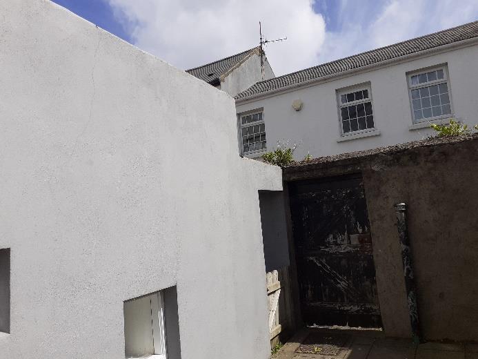 A photograph showing a high white rendered wall in the foreground and a traditional white building with sash windows in the background.