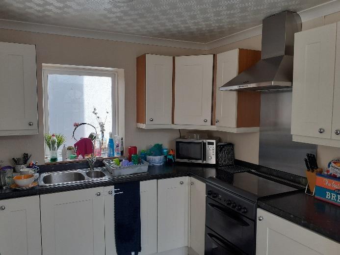 Interior photograph of a residential kitchen featuring white cabinetry, black countertops, and stainless steel appliances.