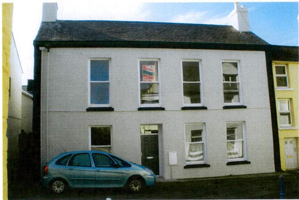 A street-level photograph of a two-story white terraced house featuring sash windows and a blue car parked in front.