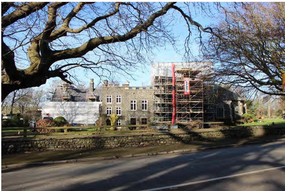 A photograph showing a large stone building, likely a chapel, covered in scaffolding and protective sheeting.