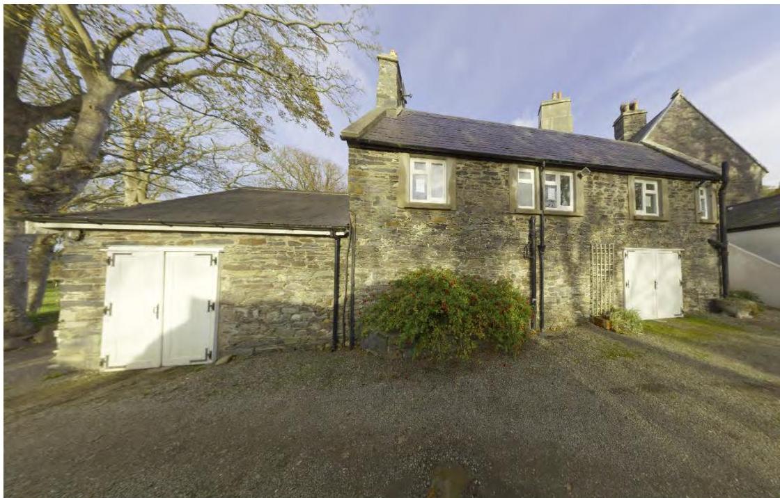 A photograph showing the exterior of a stone building complex with white double doors and a gravel driveway. The structure appears to be an old stone chapel or outbuilding in a rural setting.