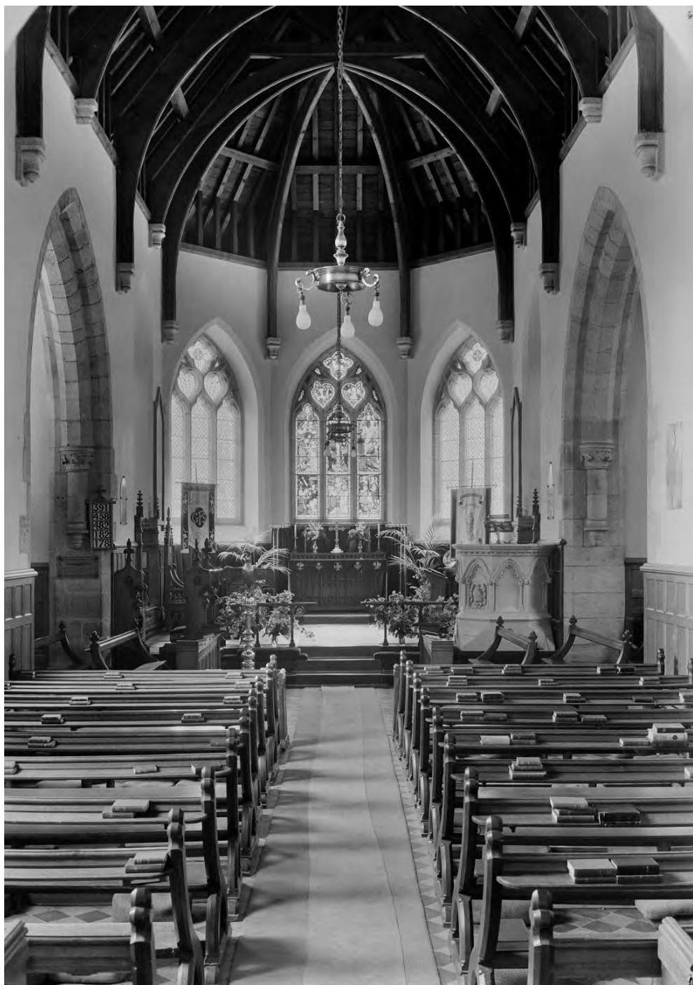 A black and white photograph showing the interior of a historic chapel, featuring rows of wooden pews, a central aisle, and a vaulted ceiling.