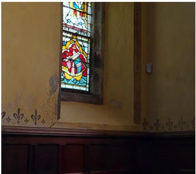 Interior photograph showing a stained glass window in a corner with yellow walls and dark wood paneling.