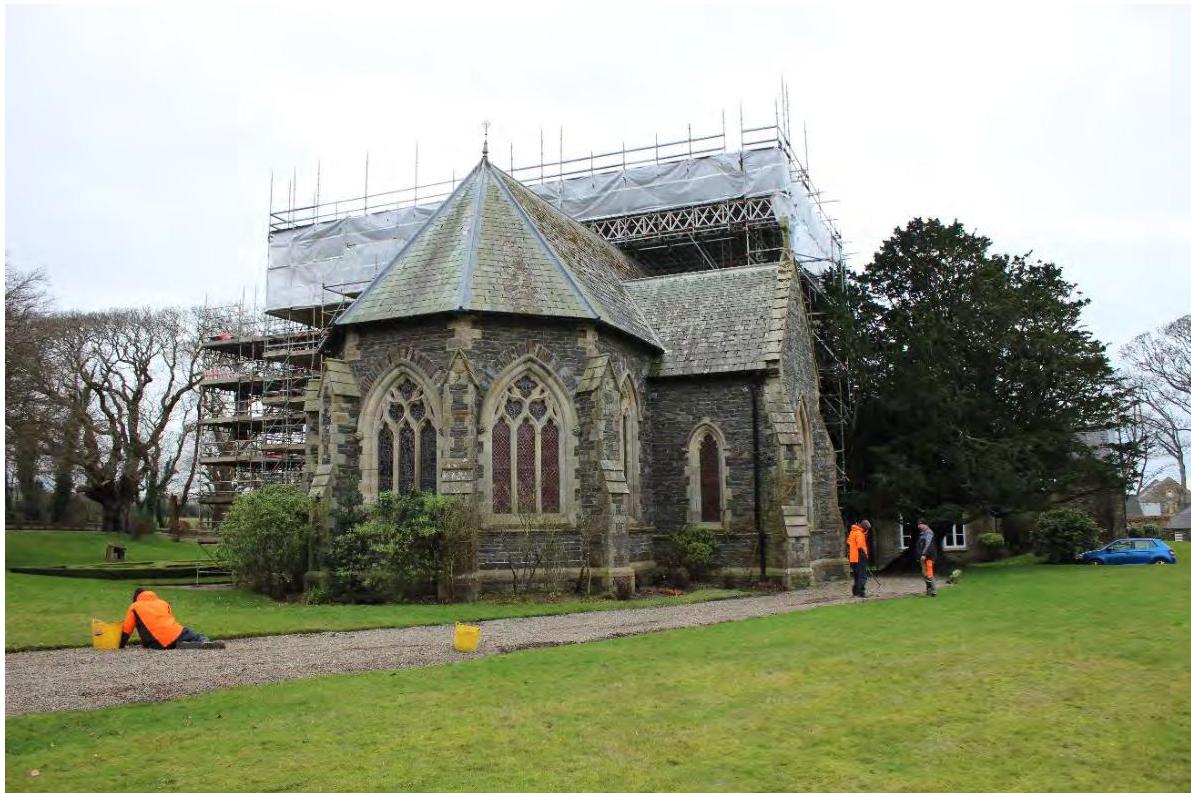 A photograph of the Chapel of St. Nicholas showing scaffolding on the roof for renovation, with workers in high-visibility clothing on the grounds.