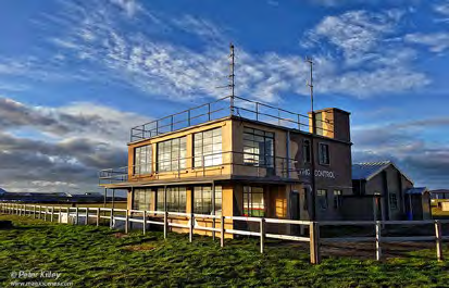 A photograph of a two-story building with a flat roof and railing, labeled 'COASTAL CONTROL', situated in a coastal setting.