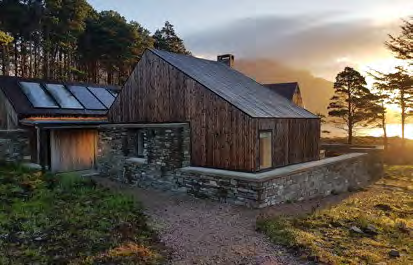 A photograph showing a modern detached dwelling with timber cladding and stone walls, situated in a rural environment with an attached garage structure.