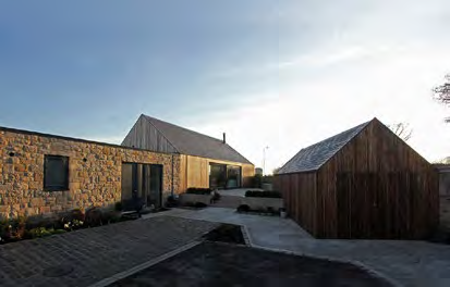 A photograph showing a modern detached dwelling with stone and timber cladding, alongside a separate wooden garage structure and paved driveway.