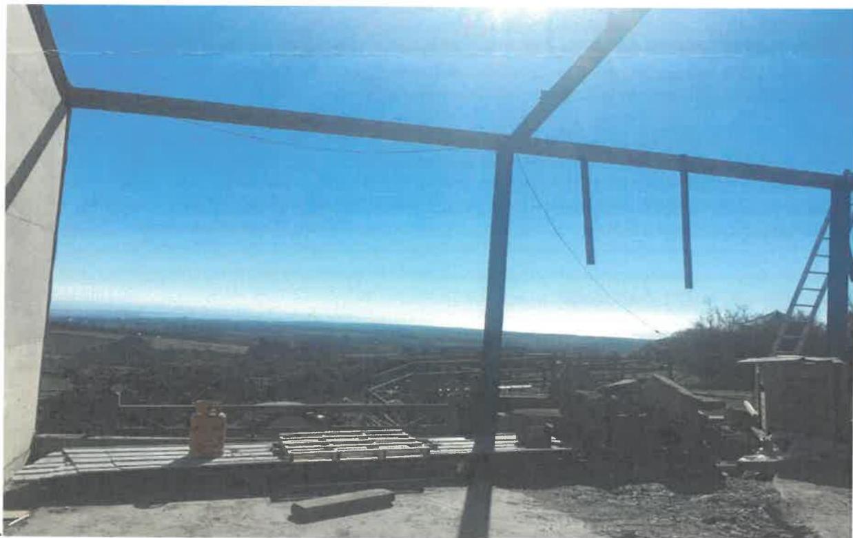 A photograph taken from inside a steel-framed structure under construction, looking out towards a coastal landscape.