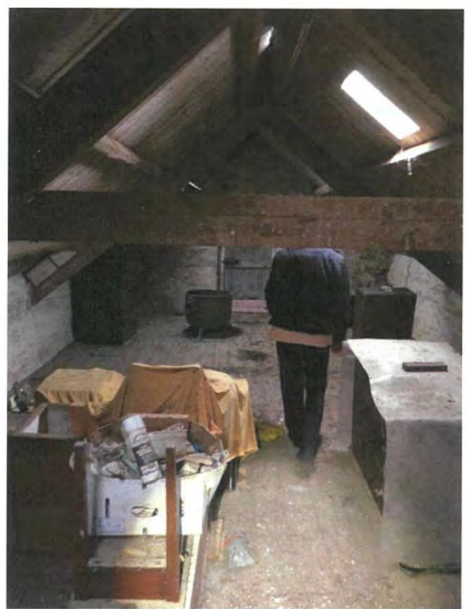 Interior photograph of a barn loft or attic space featuring exposed wooden beams, stone walls, and a skylight window.
