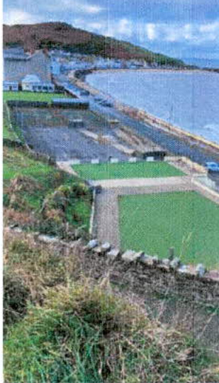 A photograph showing a coastal site with green rectangular areas, likely indicating the proposed location for tourist accommodation or a marquee near the sea wall and road.