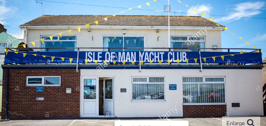 A photograph of the Isle of Man Yacht Club building showing a two-story structure with a brick and rendered facade. A blue banner with the club's name and yellow bunting are visible on the terrace level.