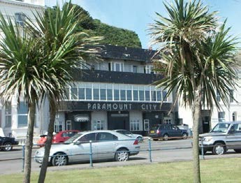 A photograph showing the exterior of a building labeled 'PARAMOUNT CITY' with palm trees and parked cars in the foreground.