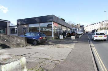 Street-level photograph of a single-story commercial building with a flat roof and large glass windows, showing a car park and street access.