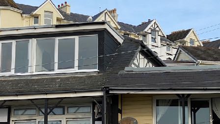A photograph showing the exterior of a residential property featuring a prominent modern two-storey extension with large windows and dark cladding.