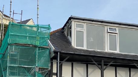 A photograph showing a residential property with a new dormer extension and scaffolding covered in green netting.