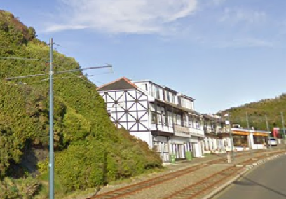 A street-level photograph showing a white building with black timber framing situated next to a railway line and a grassy embankment.