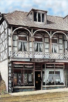 A view of a traditional timber-framed building featuring a shop front on the ground floor and a balcony with arched supports on the first floor.