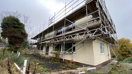 A photograph showing a two-story commercial building fully covered in scaffolding, indicating ongoing construction or renovation work.
