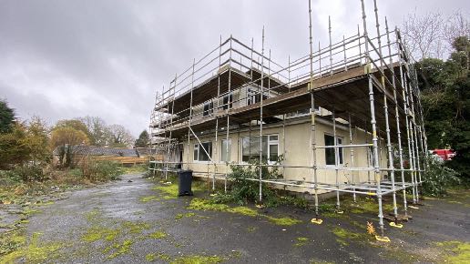 A photograph showing a two-story commercial or office building covered in scaffolding, indicating ongoing renovation or conversion work.