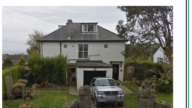 A street-level photograph of a white, two-story detached house with a slate roof and an attached garage.
