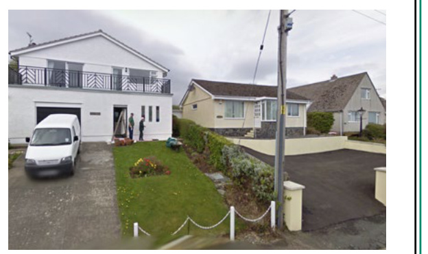 A photograph showing a white, two-story detached house with an integral garage on the left, with workers standing near the entrance and a white van parked in the driveway.