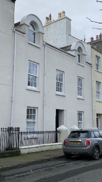 A street-level photograph showing the white facade of a terraced building with sash windows and white downpipes.