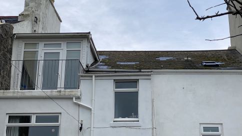 The image shows the upper exterior of a white residential building featuring a pitched roof with visible dark patches, a stone chimney stack, and white guttering.
