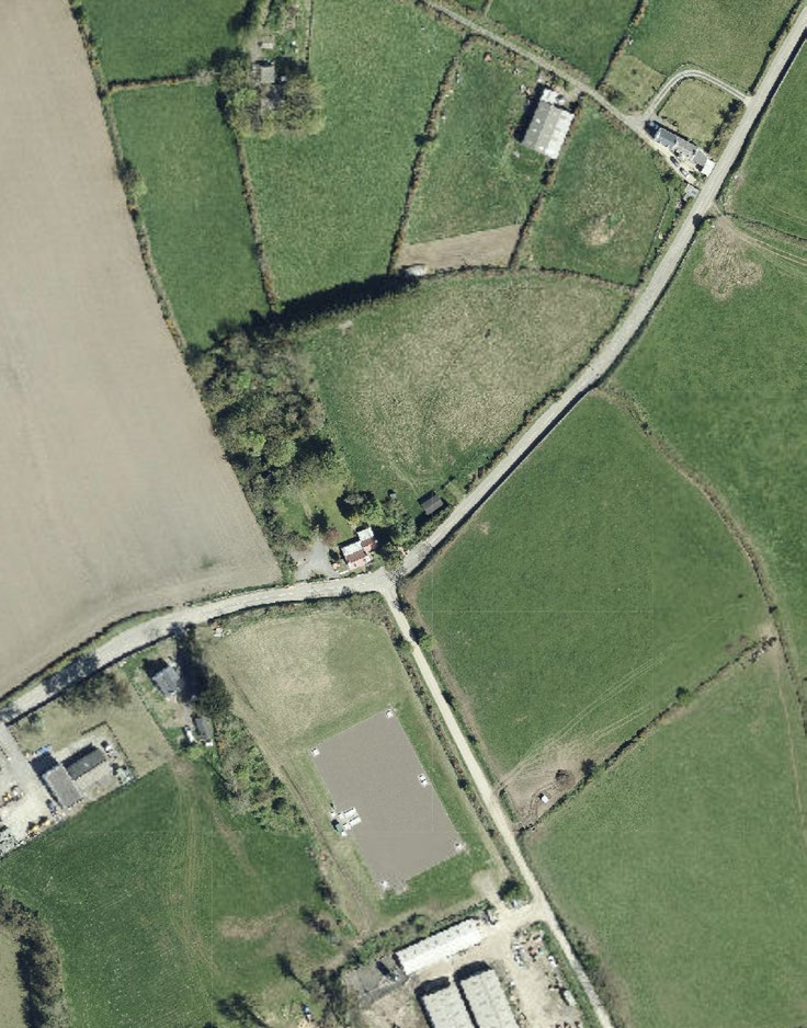 Aerial view of a rural site showing agricultural fields, hedgerows, and existing buildings near a road junction.