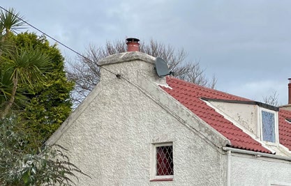 A low-angle photograph showing the exterior elevation of a white rendered building with a red tiled roof, featuring a chimney stack and satellite dish.