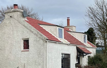 A photograph of a white rendered single-story dwelling with a red tiled roof and dormer windows.