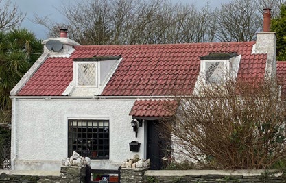 A photograph of a white, single-story detached house featuring a red tiled roof with dormer windows and a stone boundary wall.