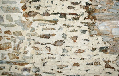 A close-up photograph of a traditional rough stone wall with white mortar or render, likely part of an existing rural building.