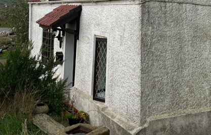 A close-up photograph showing the exterior corner of a white-rendered building featuring a diamond-paned window and a small tiled porch overhang.