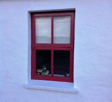 A close-up photograph of a red-framed window set into a white rendered wall, with items visible on the interior sill.