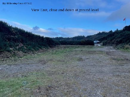 A ground-level photograph showing a grassy clearing or field bordered by trees, likely the site of the proposed shooting range facilities.