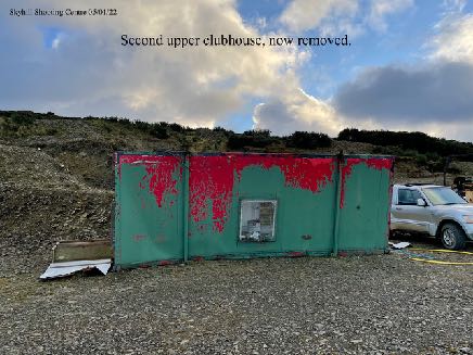 A photograph showing a weathered green and red prefabricated structure on a gravel site, with text overlay indicating it is a removed clubhouse.