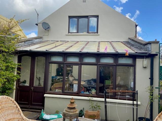 A photograph showing the rear elevation of a residential property featuring a single-story conservatory extension with a translucent roof and a satellite dish on the upper wall.