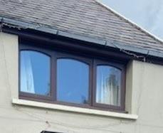 A close-up photograph showing a three-pane window with arched tops set into a cream rendered wall beneath a slate roof.