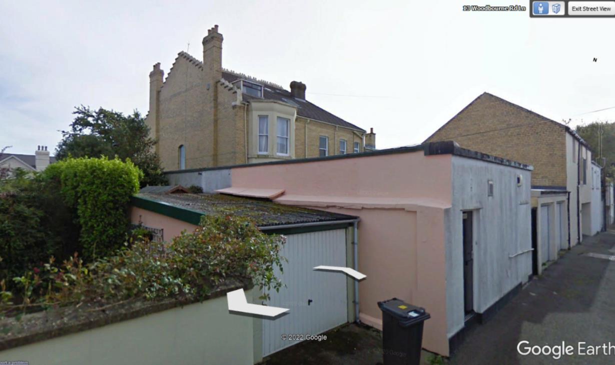 A Google Earth street view image showing a residential property with a large two-story house and a single-story outbuilding or garage in the foreground.