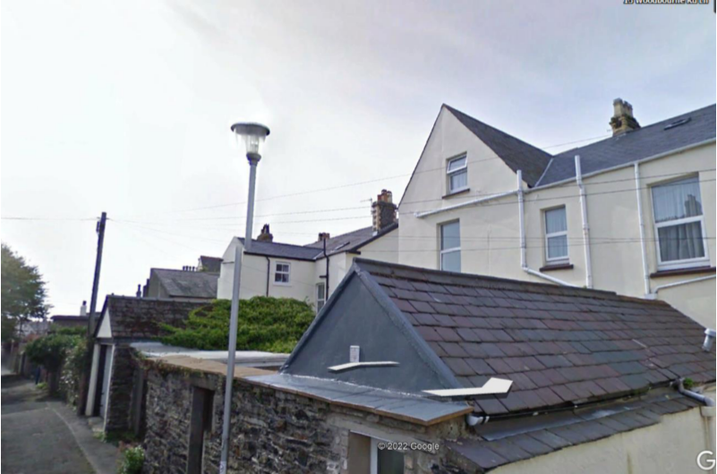 A street-level photograph showing a row of residential buildings with slate roofs and stone walls, featuring a street lamp in the foreground.