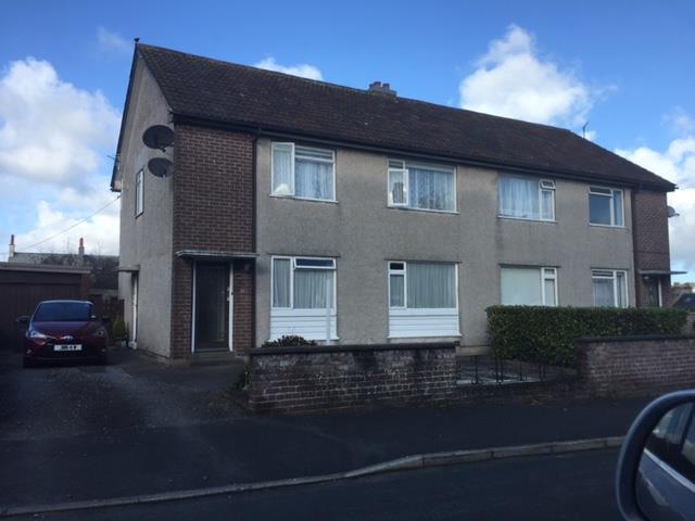A photograph showing the front elevation of a two-story semi-detached house with a visible chimney stack on the roof ridge. A car is parked in the driveway to the left.