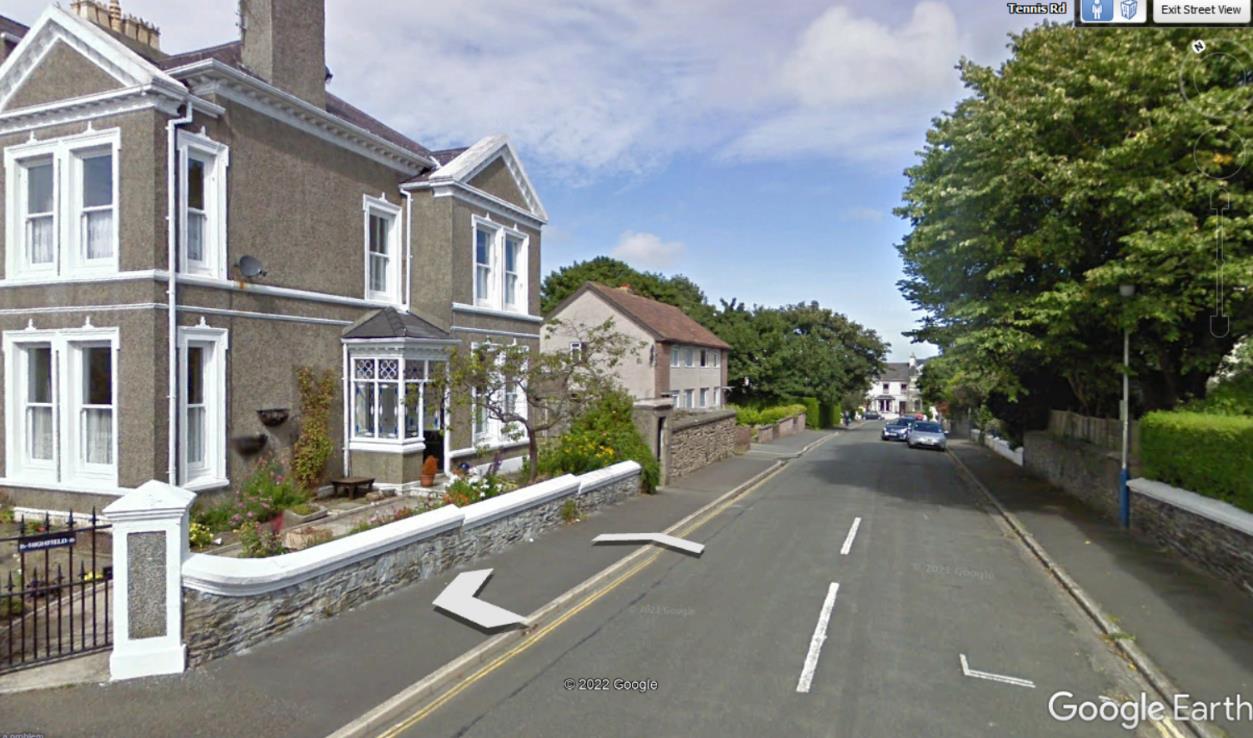 A Google Earth Street View screenshot showing a two-story detached house with a chimney stack and stone boundary wall on a residential street.